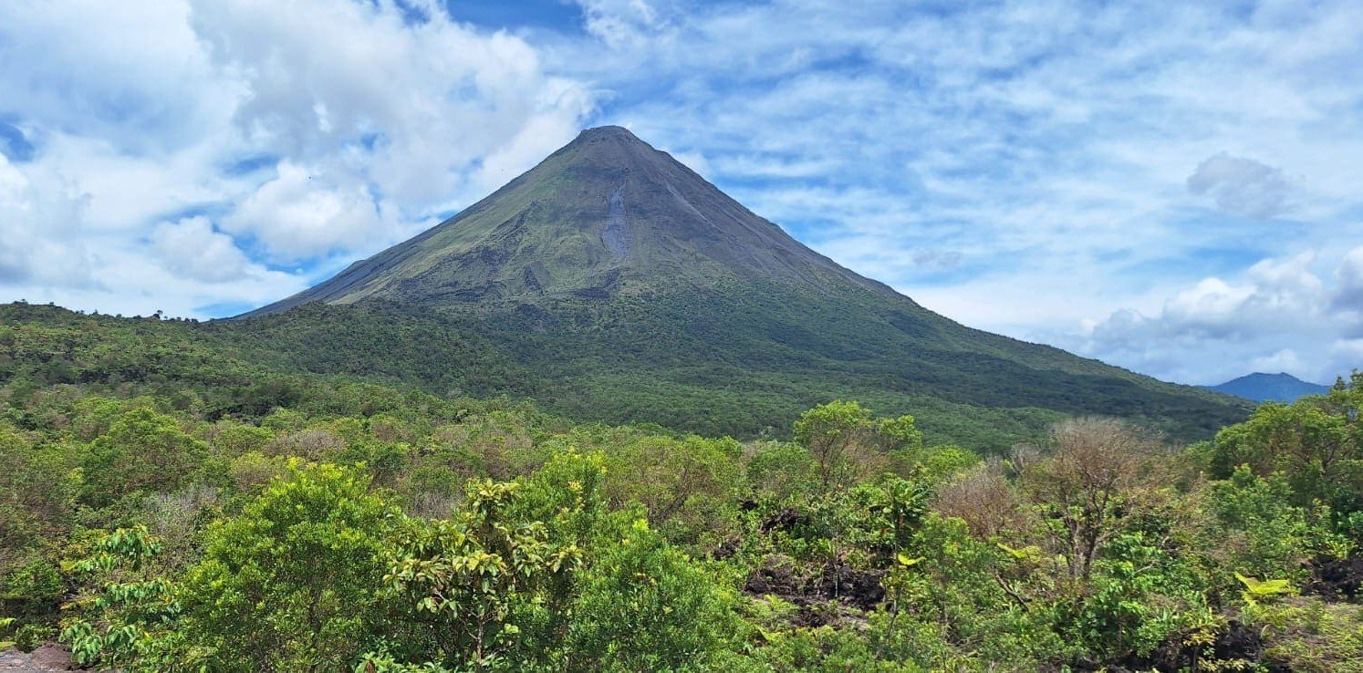 An unobstructed view of the Arenal Volcano, surrounded by a blue sky and clouds moving at the top.